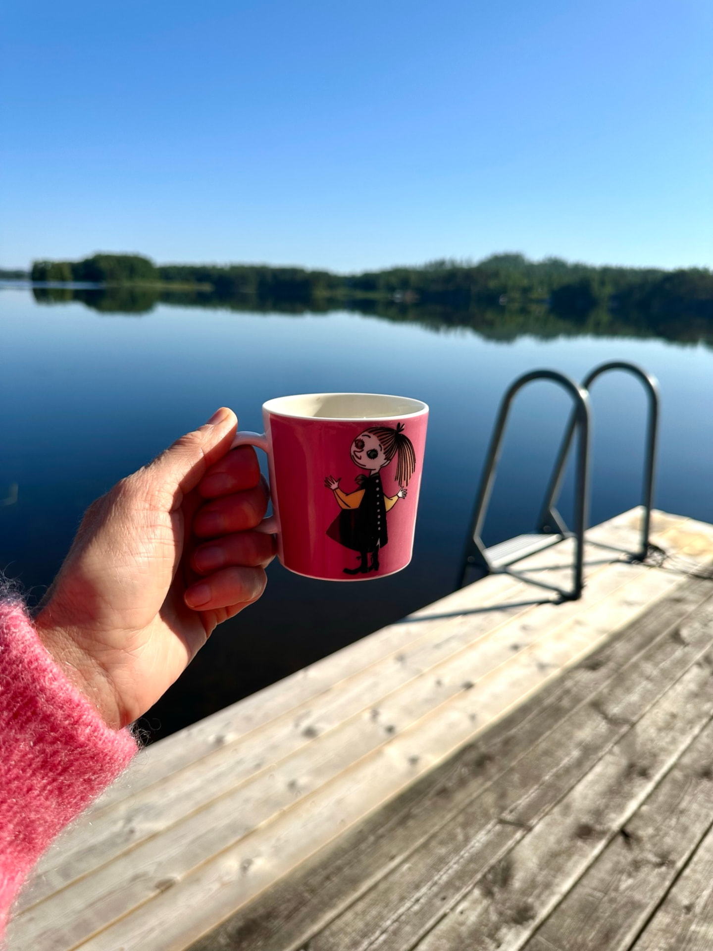 A cup of coffee held on the jetty above still lake water