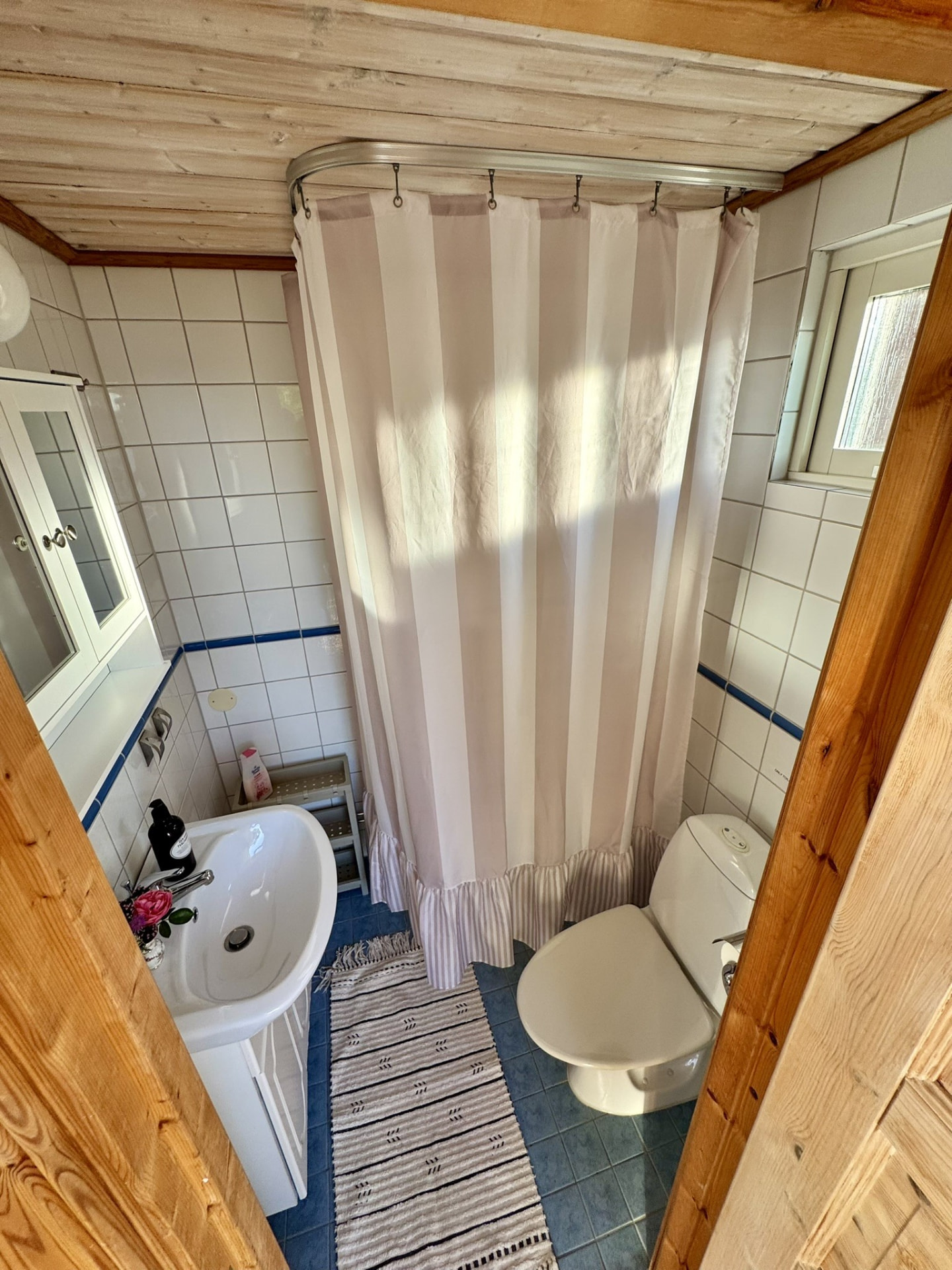 The small tiled bathroom with shower, basin and rag rug