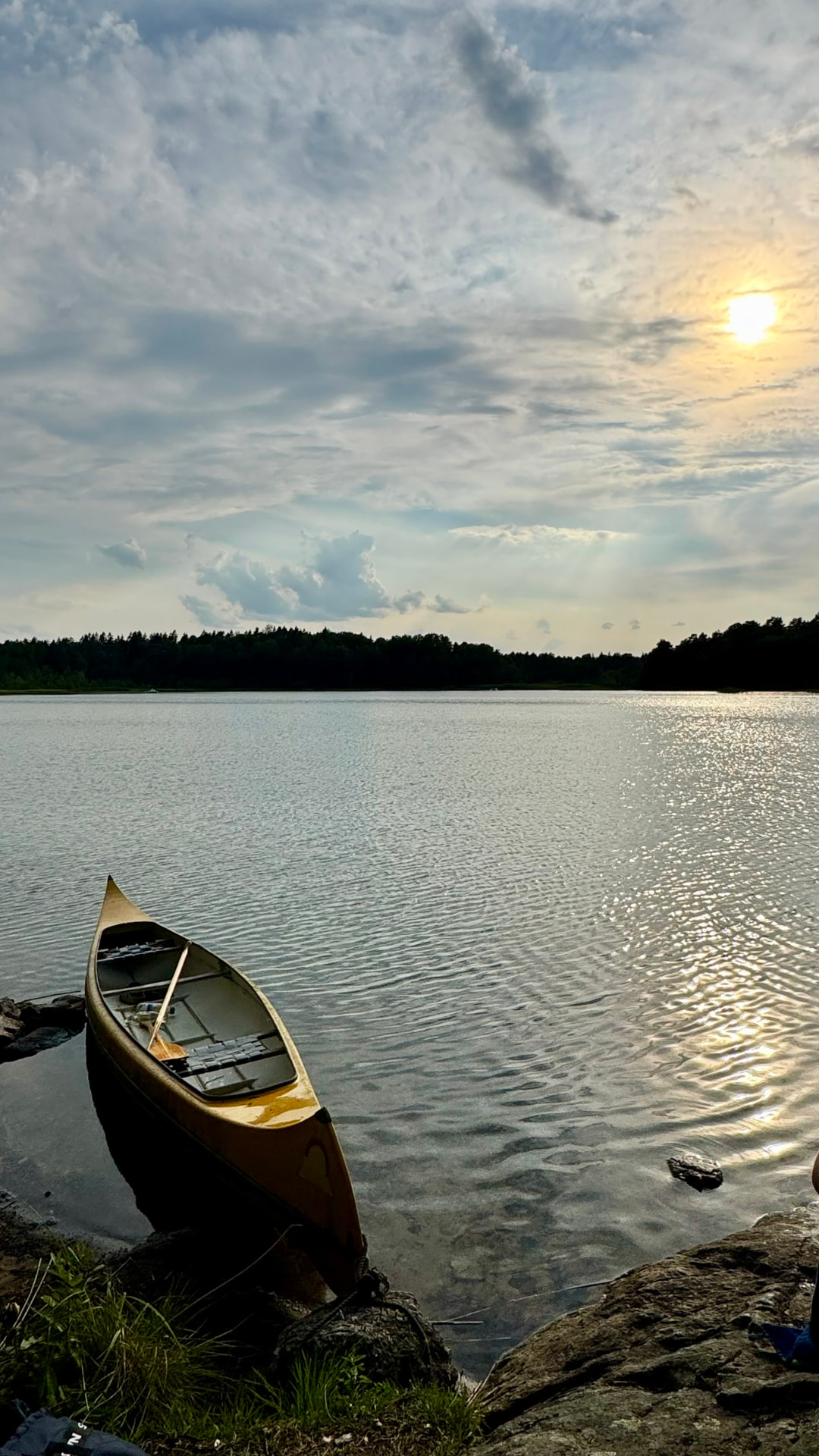 A wooden canoe pulled up on the rocks at the water's edge at sunset